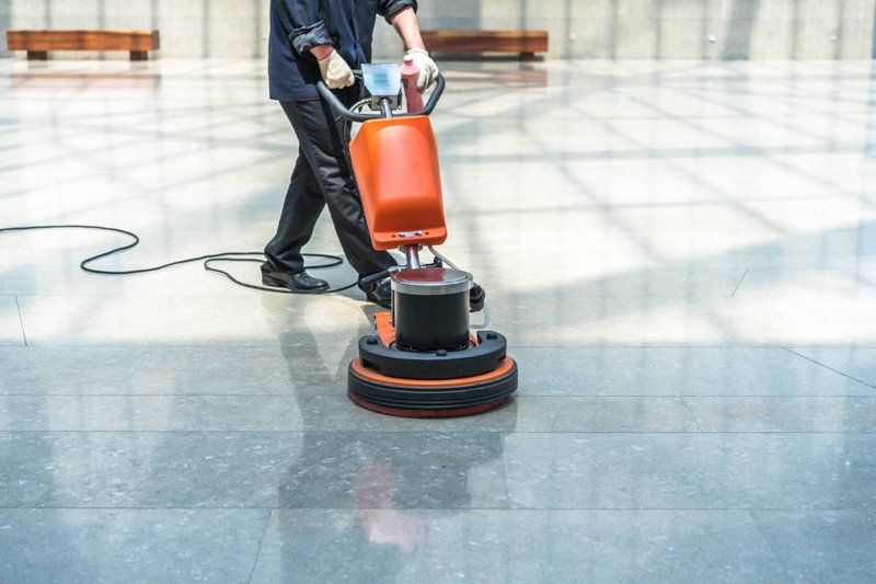 Worker guiding a floor buffer across polished stone floors