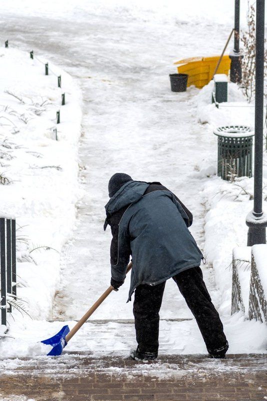 Worker shoveling snow from a walkway alongside a property